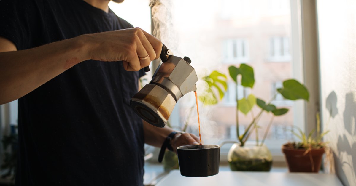 How Coffee Sample Packs Help You Find the Best Iced Brew A man in a black T-shirt stands at his kitchen counter as he pours freshly brewed moka pot coffee into a coffee mug.