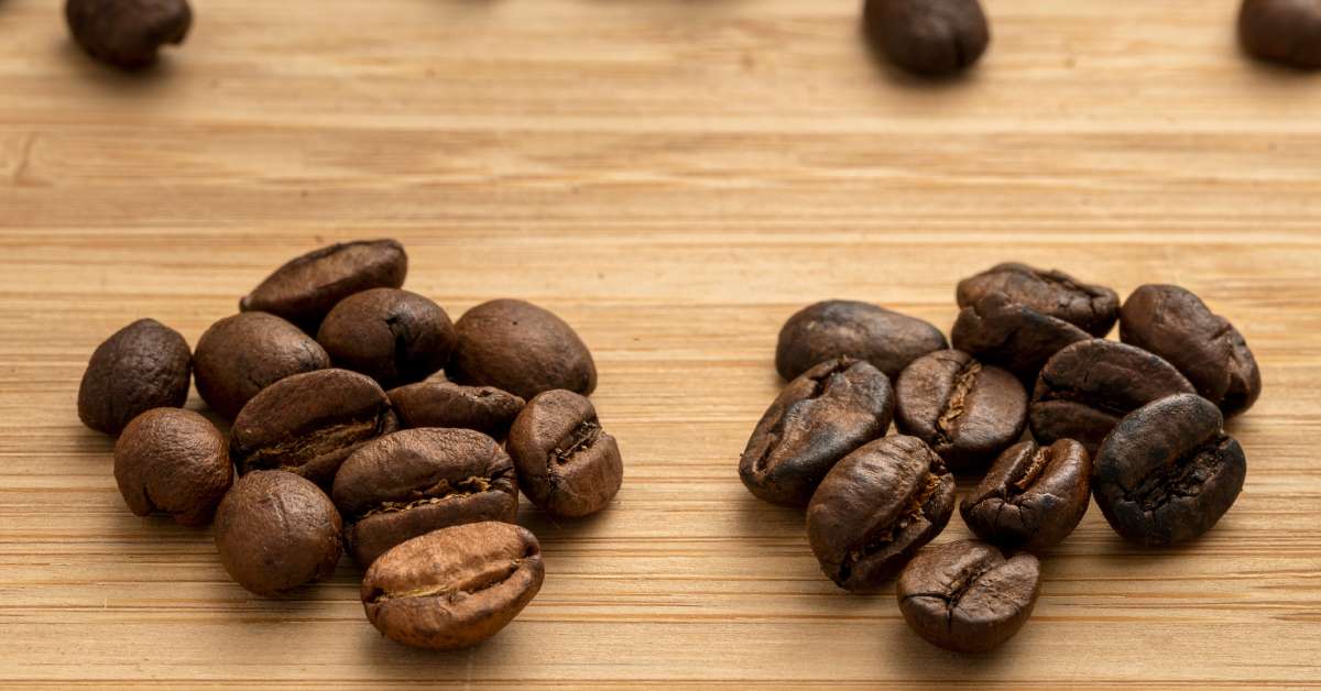 Two small piles of coffee beans sitting on a wooden table. On the left is a medium roast and on the right is a dark roast.