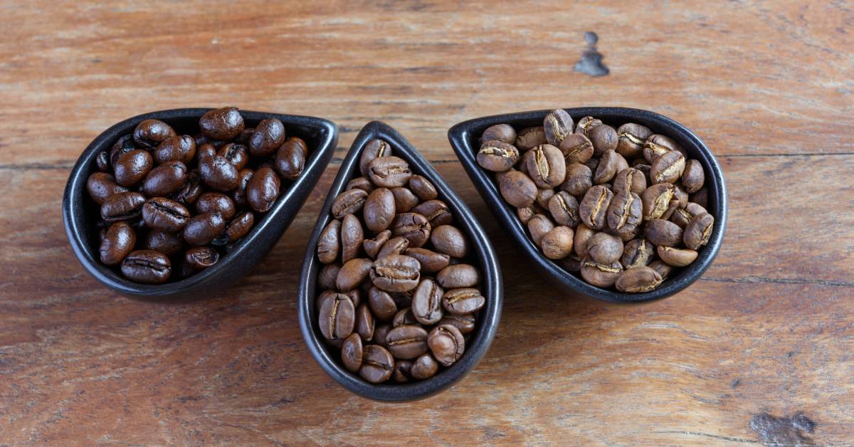 Three black teardrop-shaped bowls sit next to each other. Each bowl holds a different color of coffee beans.