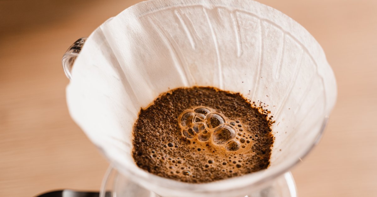 A pour over coffee system up close with the filter full of coffee grounds and freshly brewed hot water bubbling on top.