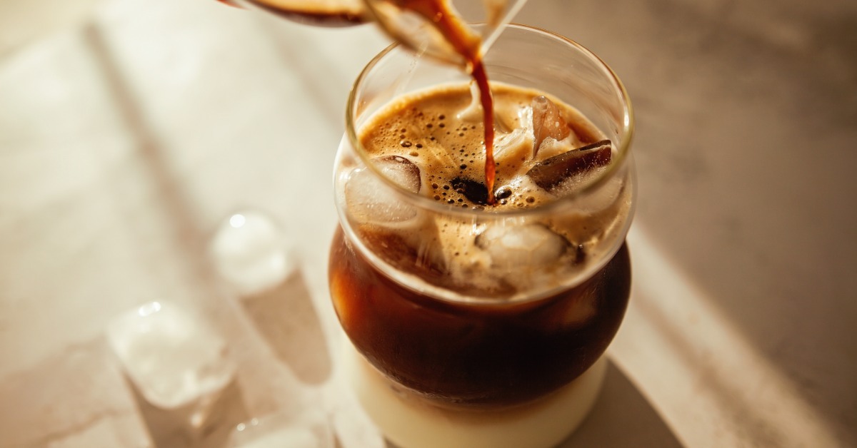 A close-up of a morning iced coffee sitting on the kitchen counter. Someone pours coffee into the glass. A close-up of a morning iced coffee sitting on the kitchen counter. Someone pours coffee into the glass.